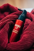 A red bottle labeled 'MARO 17 COLLAGEN SHOT' is nestled in a soft, textured red fabric. The bottle features a pump top, and the vibrant red of the fabric complements the glossy finish of the bottle.