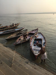 A serene early morning shot of the Ganga riverbank in Varanasi, with boats gently floating and pilgrims beginning their day.