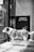 A dog with a white and brown coat stands patiently at the entrance of a store, its gaze directed through the glass door. The dog is wearing a harness and leash. Behind it, a sign with text in a foreign language is visible against the store front.