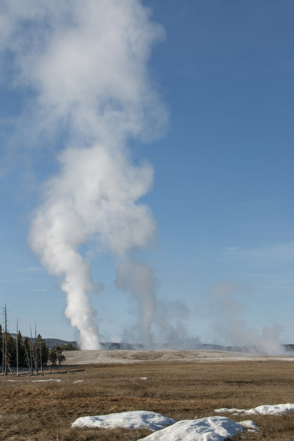 a large cloud of smoke with Old Faithful in the background