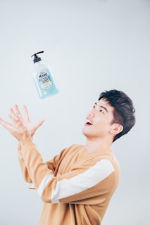 A person wearing a camel-colored sweater with white stripes on the sleeves appears to be playfully tossing or catching a bottle of Maro 3D Hair Volume shampoo. The individual is smiling and looks engaged in the activity.