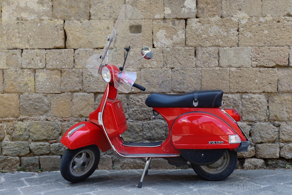 a red scooter parked next to a stone wall