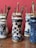 Several ornate ceramic jars, each decorated with intricate blue patterns on a white background, hold collections of paintbrushes. The jars are arranged on a wooden surface against a red wall.