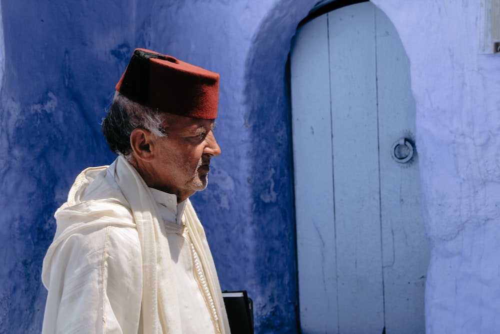 a man in a white robe and cap looking at a blue wall