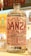 A clear glass bottle with a detailed label featuring the text 'Danza de los Pajaros'. The label includes various information such as alcohol content and origin. The bottle is surrounded by glass cups on a bar counter with a colorful, patterned background.