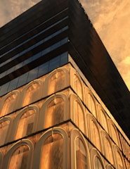A sleek, modern building facade featuring glass and aluminum elements reflecting the golden hues of sunset in Al Khobar.