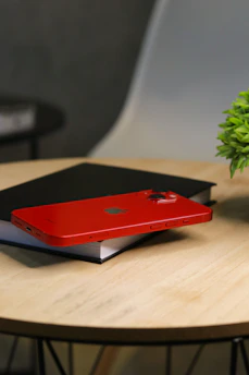 A sleek smartphone resting on a wooden desk beside a notebook and pen, bathed in soft natural light.