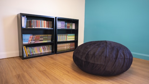 a black bean bag on a wood floor in front of a bookcase
