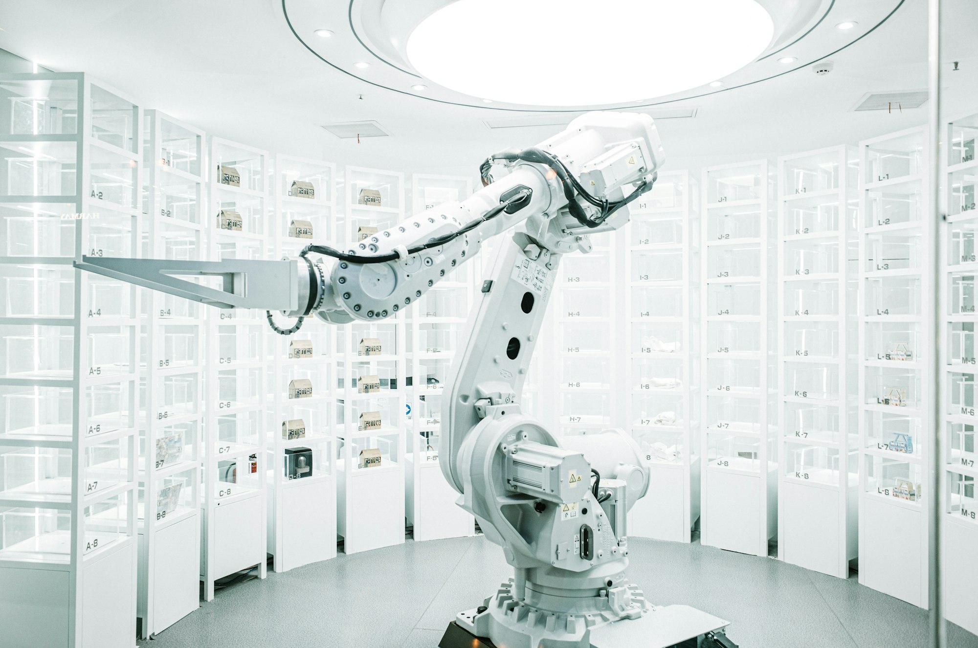 a large white robotic arm in a semicircular room of open white cabinets