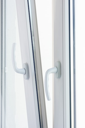 Two white window handles are positioned side by side on a slightly open window, catching soft, diffused daylight. The handles are modern in design, made of what appears to be plastic or painted metal.