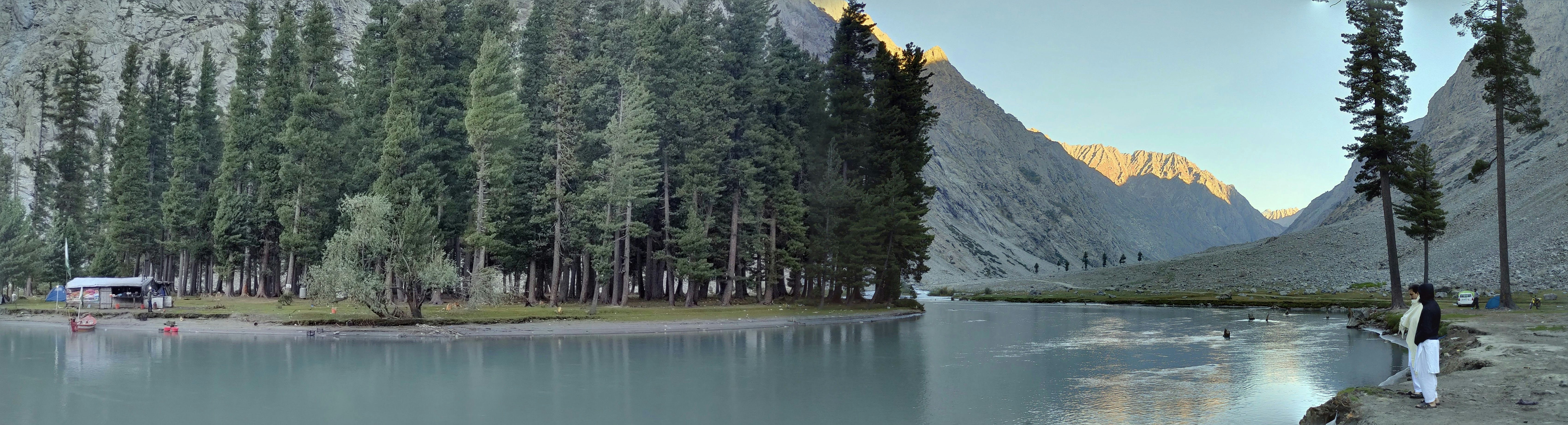 a person standing next to a lake with trees and mountains in the background