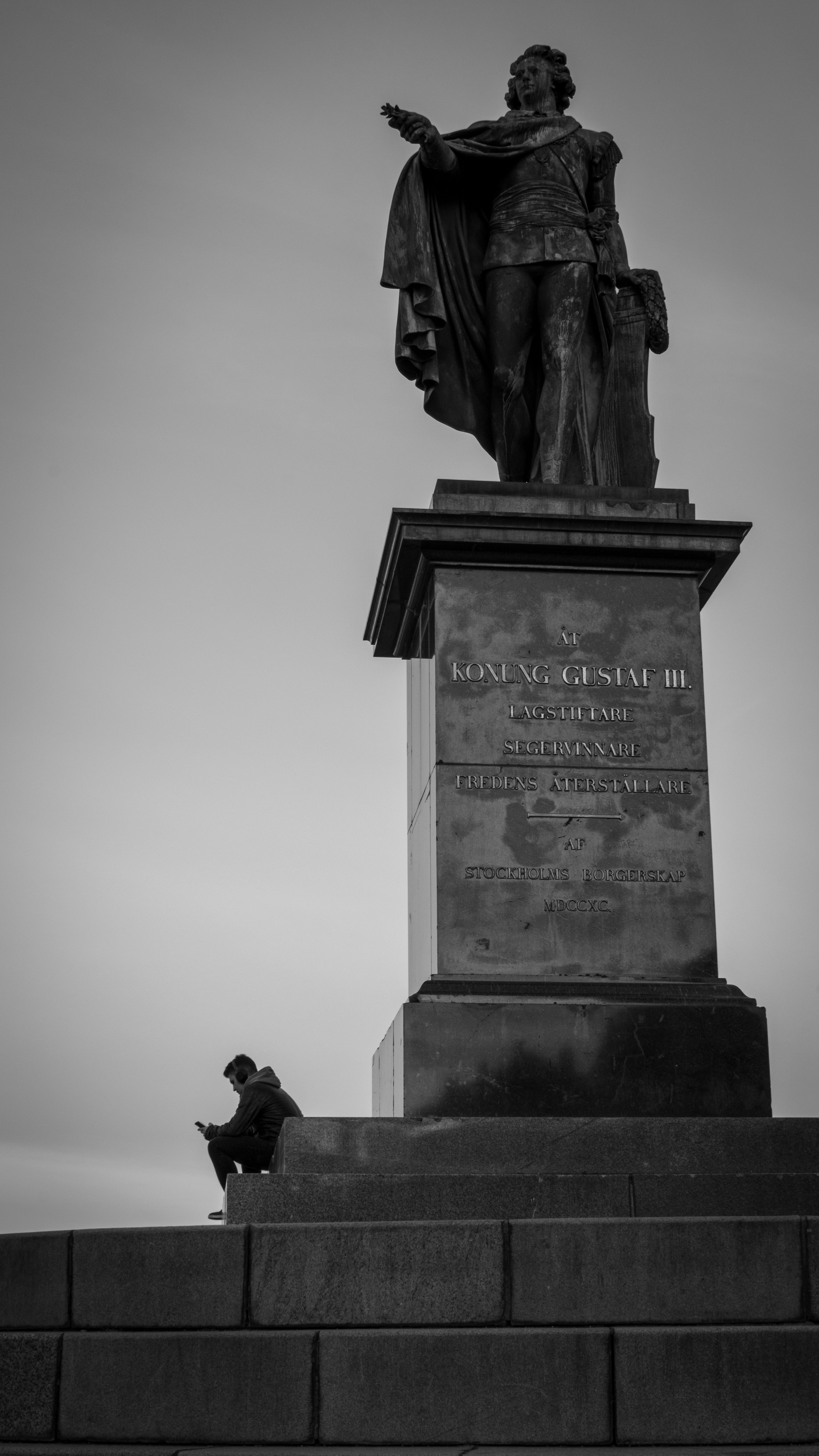 Uomo seduto sui gradini della statua guardando il telefono