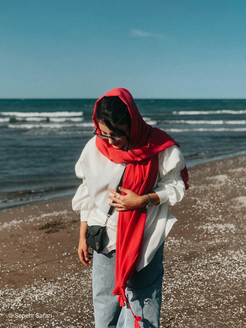 a man wearing a red scarf and a white jacket on a beach