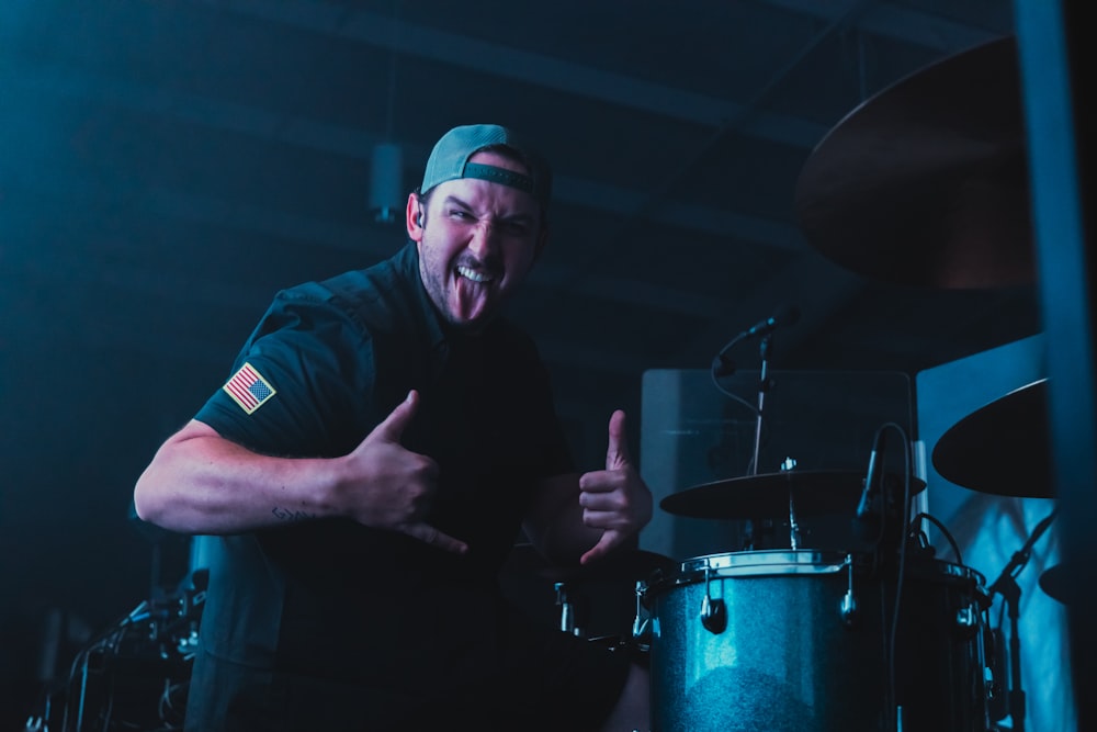 a man with a hat and a microphone in front of a drum set