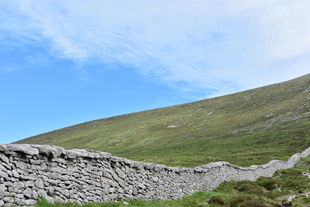 a stone wall in front of a grassy hill