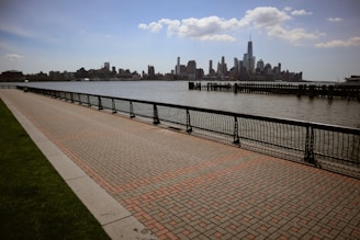 a brick walkway next to a body of water with a city in the background