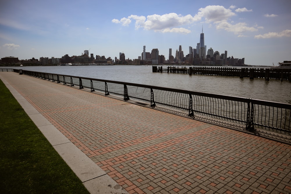 a brick walkway next to a body of water with a city in the background