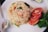 A plate features a serving of fried rice with visible vegetables such as diced carrots and leafy greens. Next to the rice are slices of fresh tomato and a garnish of green lettuce. A metal spoon is placed beside the dish, and a wedge of lime is partially visible in the corner.
