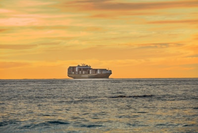 A modern cargo ship sailing through calm ocean waters at sunrise.
