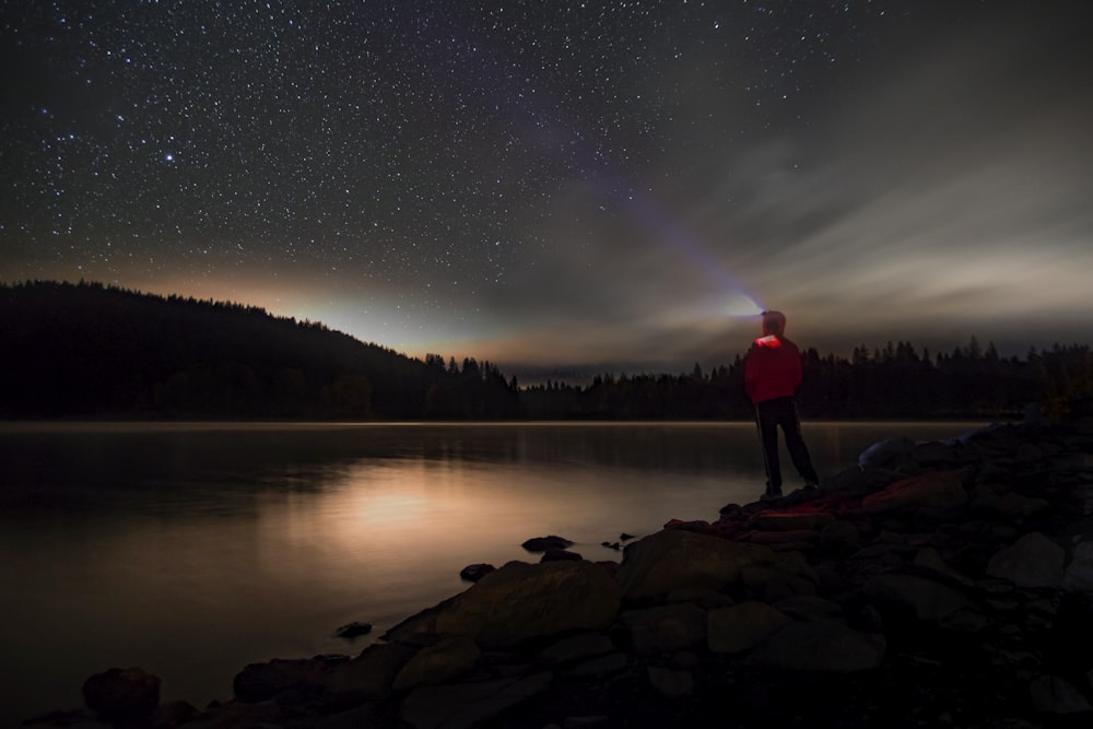 a person standing on a rocky shore with a body of water and stars in the sky