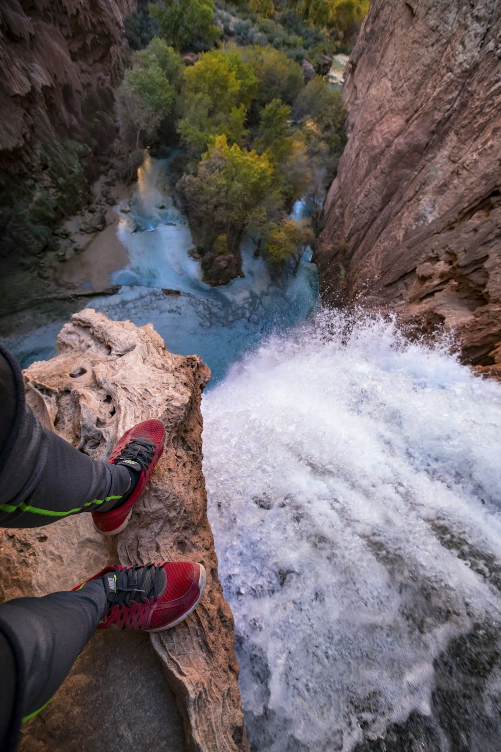 a person's feet on a rock ledge above a river
