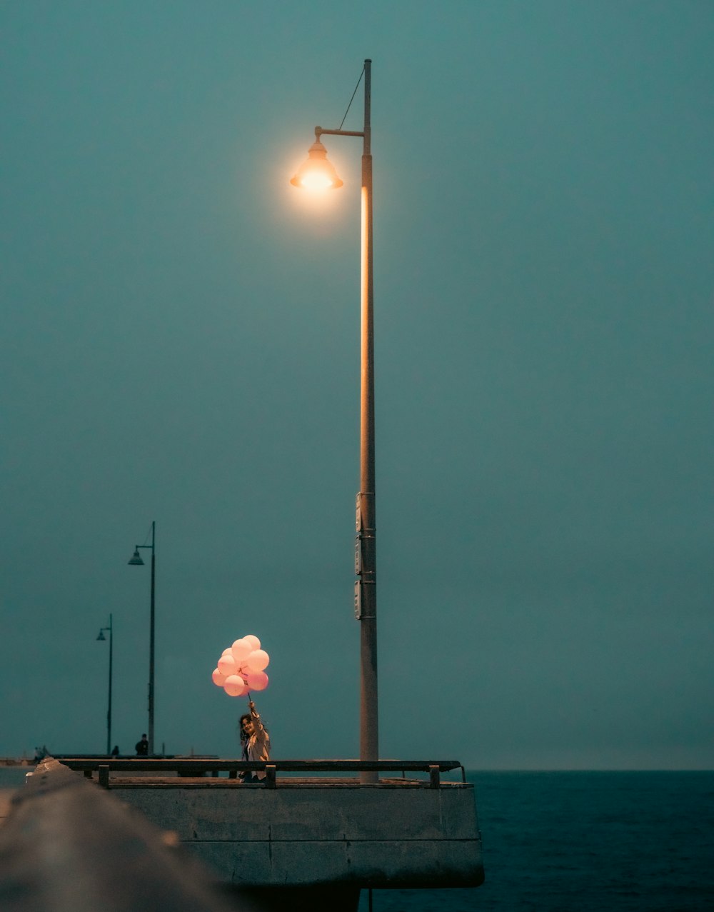 a person holding a pink balloon on a dock with a body of water in the background