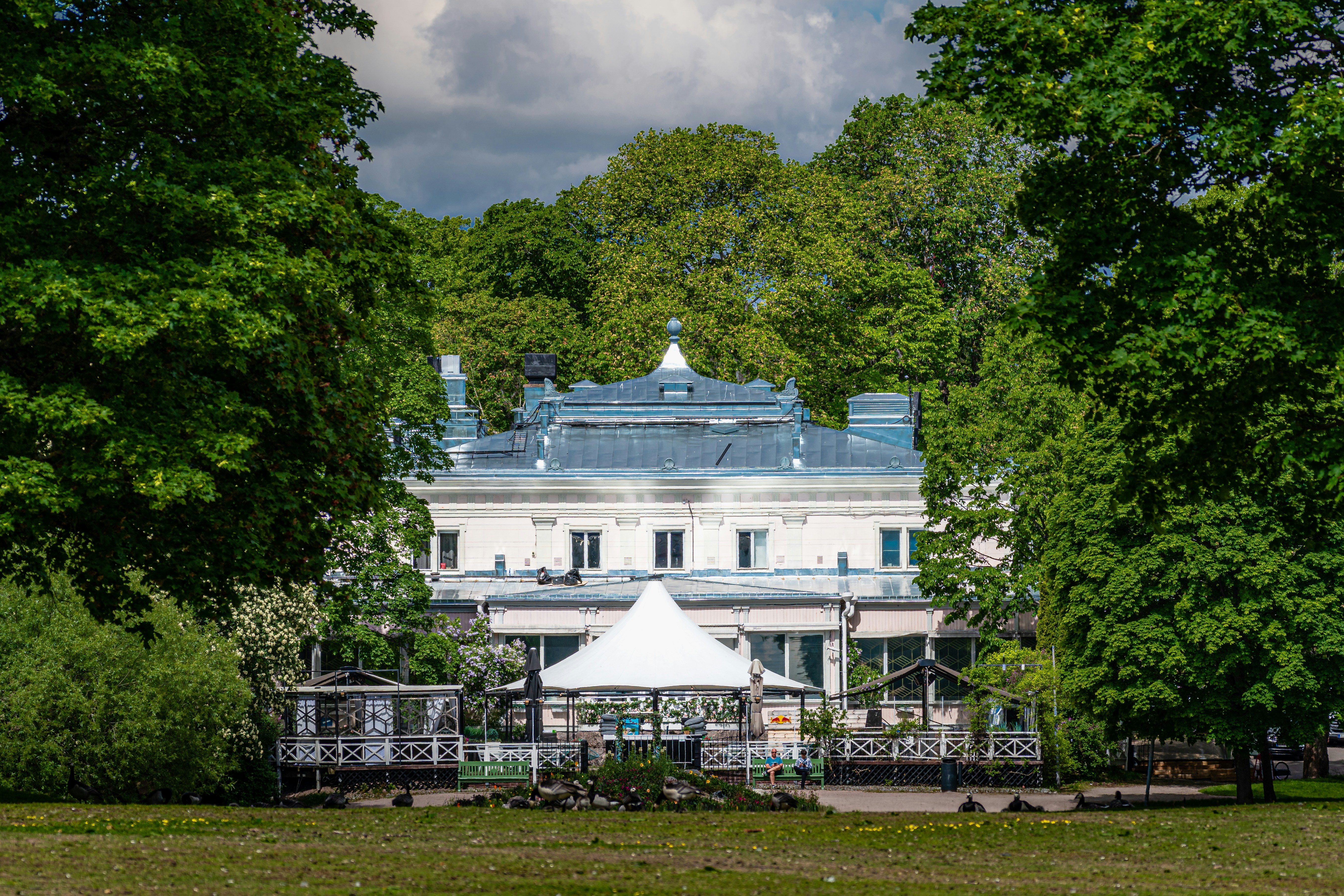 a large white building with a blue roof surrounded by trees
