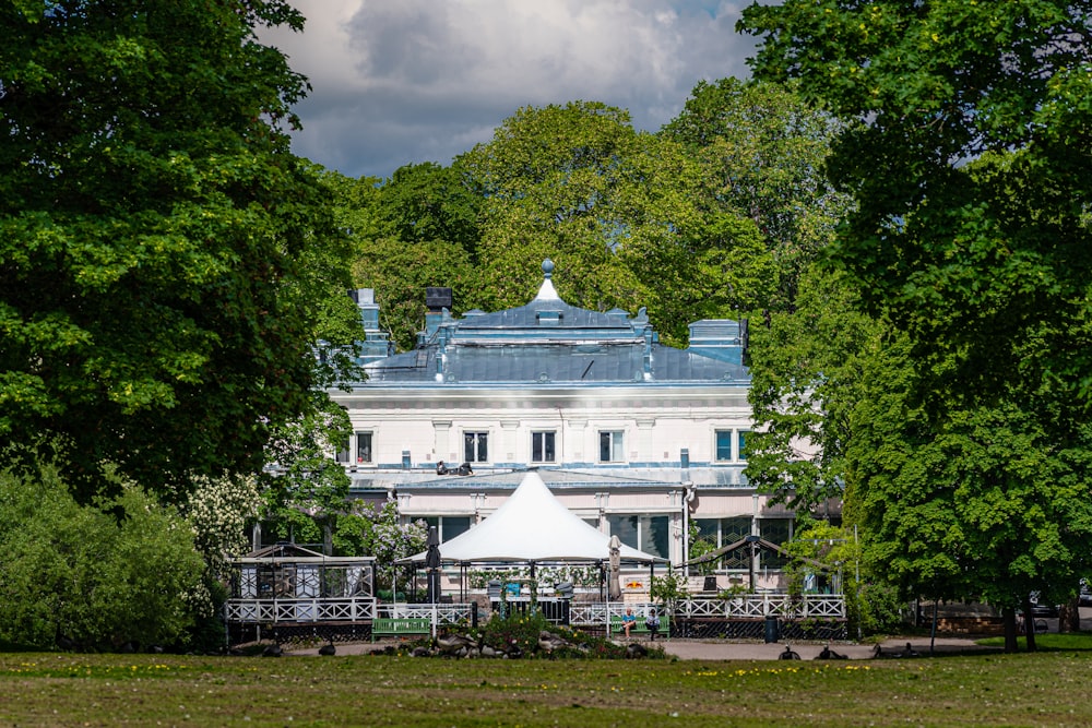 a large white building with a blue roof surrounded by trees