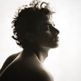 A silhouette of a person with curly hair gazing upwards into the light. The image has a soft, ethereal quality with gentle contrasts between the dark figure and the bright background.