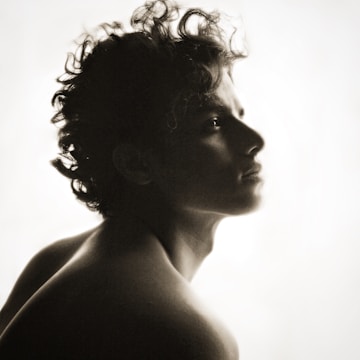 A silhouette of a person with curly hair gazing upwards into the light. The image has a soft, ethereal quality with gentle contrasts between the dark figure and the bright background.
