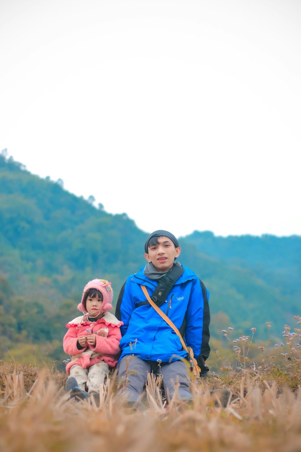 a man and a child sitting on a hill with mountains in the background