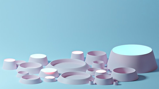 A collection of various pastel-colored cylinders and cone-shaped objects arranged against a light blue background. The objects have a soft, smooth texture and gentle lighting creates subtle shadows.