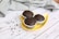 Three chocolate muffins with chunks of chocolate are placed on a yellow leaf-shaped plate. The plate sits on a white wooden surface, accompanied by scattered chocolate chips. A textured gray cloth is casually draped in the background.