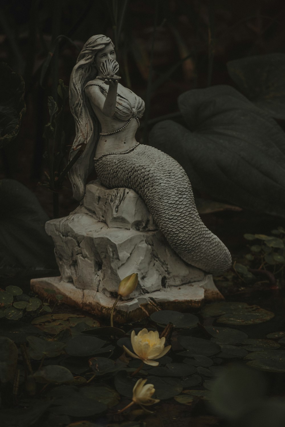 uma estátua de uma pessoa sentada em uma rocha em uma lagoa