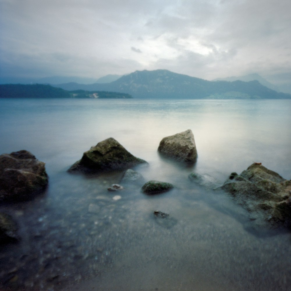 a body of water with rocks in it and mountains in the background