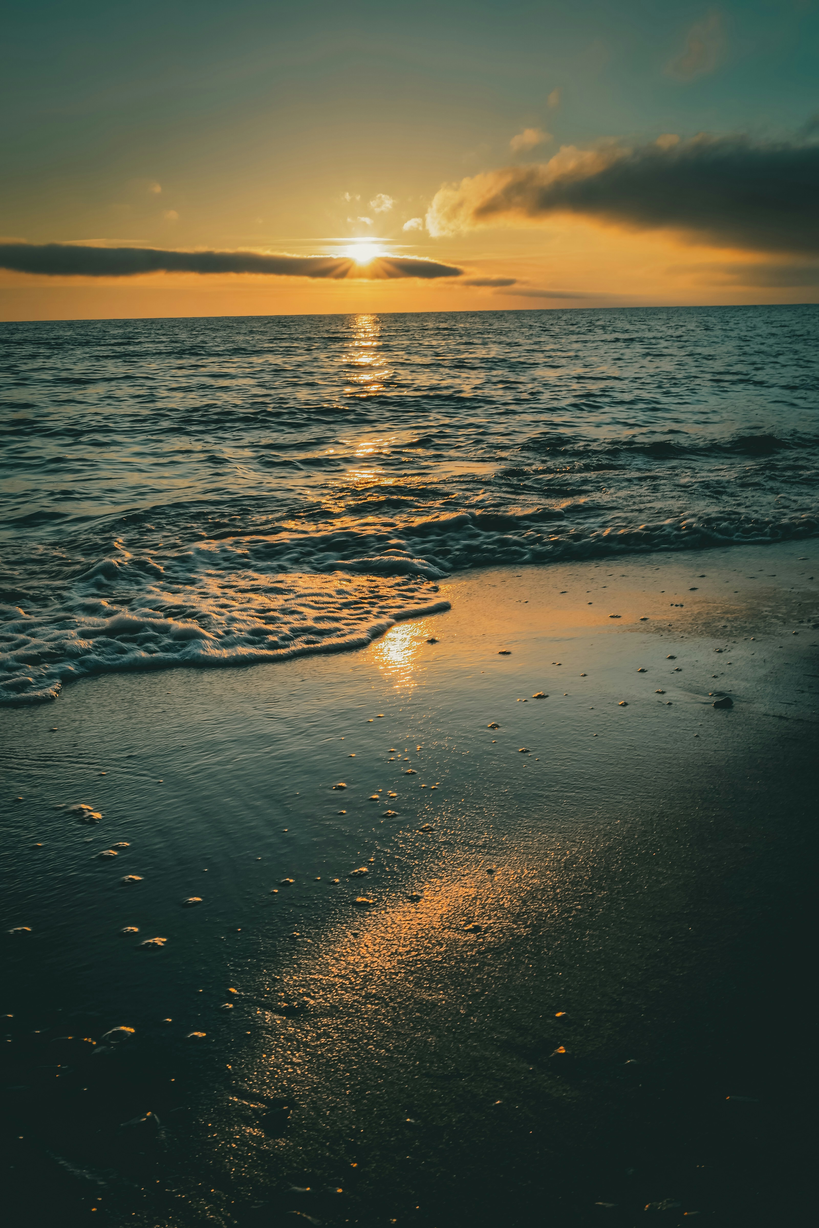 a beach with waves and the sun setting