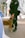 A person wearing a uniform with tactical gear is securely holding a brown K-9 dog on a leash. The setting appears to be a dock or pier with metal railings and water in the background. The dog is wearing a collar labeled 'USCG K-9' and seems calm and attentive.