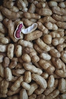 A collection of unshelled peanuts is scattered across the surface, with one peanut opened to reveal its reddish-brown seeds. The textured shells create a rough and natural pattern throughout the image.