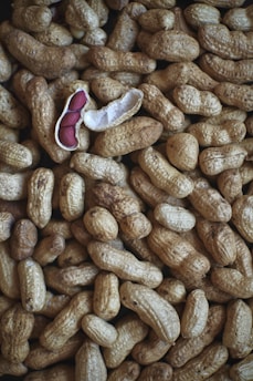 A collection of unshelled peanuts is scattered across the surface, with one peanut opened to reveal its reddish-brown seeds. The textured shells create a rough and natural pattern throughout the image.