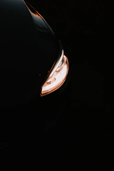 Close-up of a sleek car headlight glowing bright white LED light at dusk.