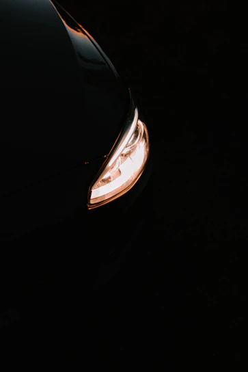 Close-up of a sleek car headlight glowing warmly in a dark garage setting