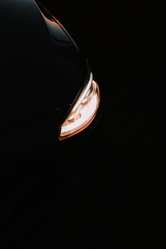 Close-up of a sleek car headlight glowing brightly on a dark road at night