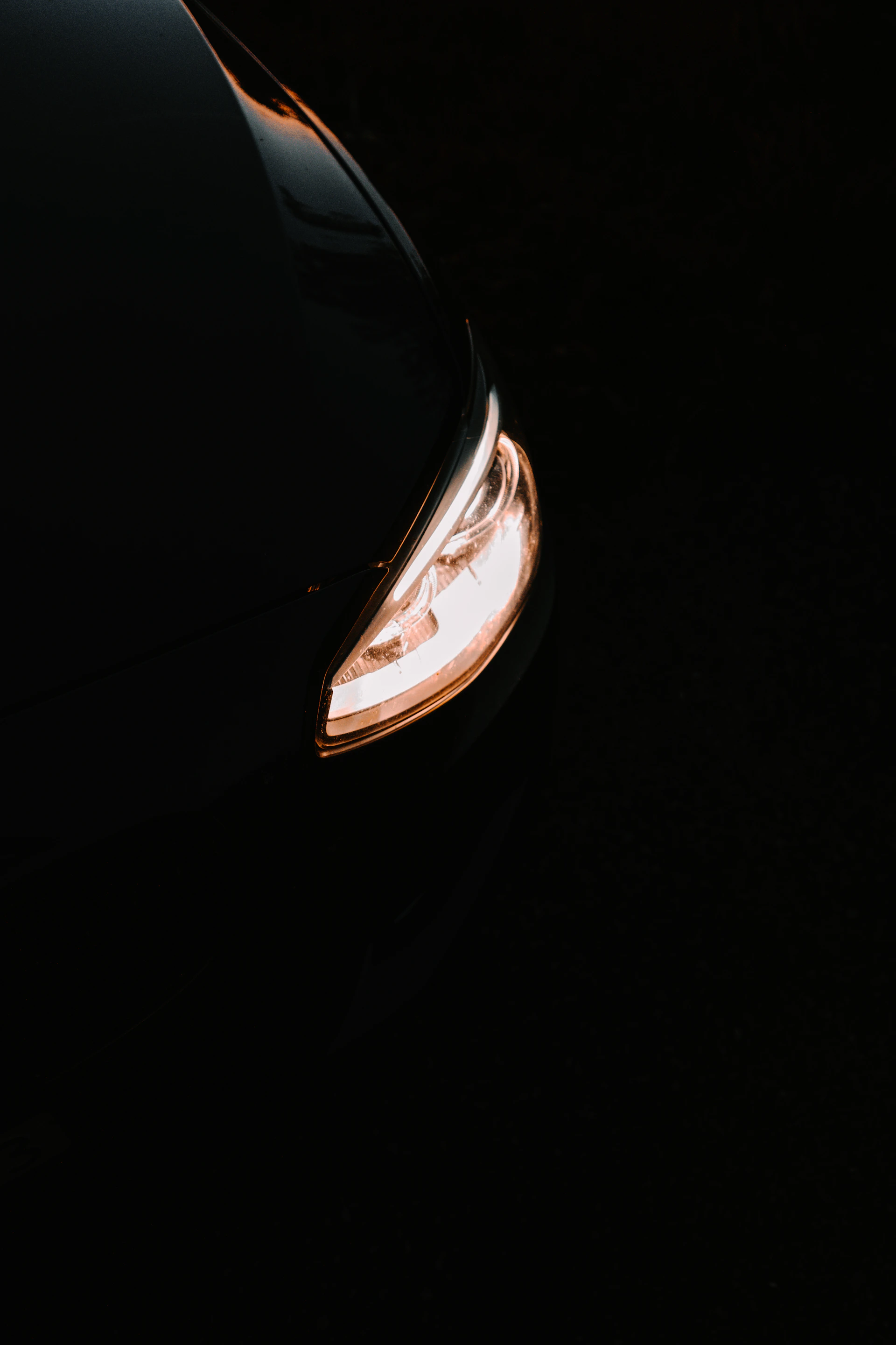 Close-up of a sleek car headlight glowing with bright white LED light on a dark street.