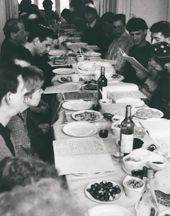 A community gathering around a wooden table sharing bread and stories, with apricot-colored textiles in the background.