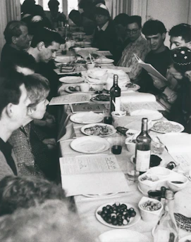 A diverse group of people smiling and sharing a meal around a large communal table.