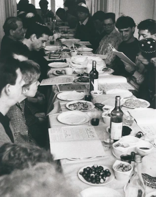 A community gathering around a wooden table sharing bread and stories, with apricot-colored textiles in the background.