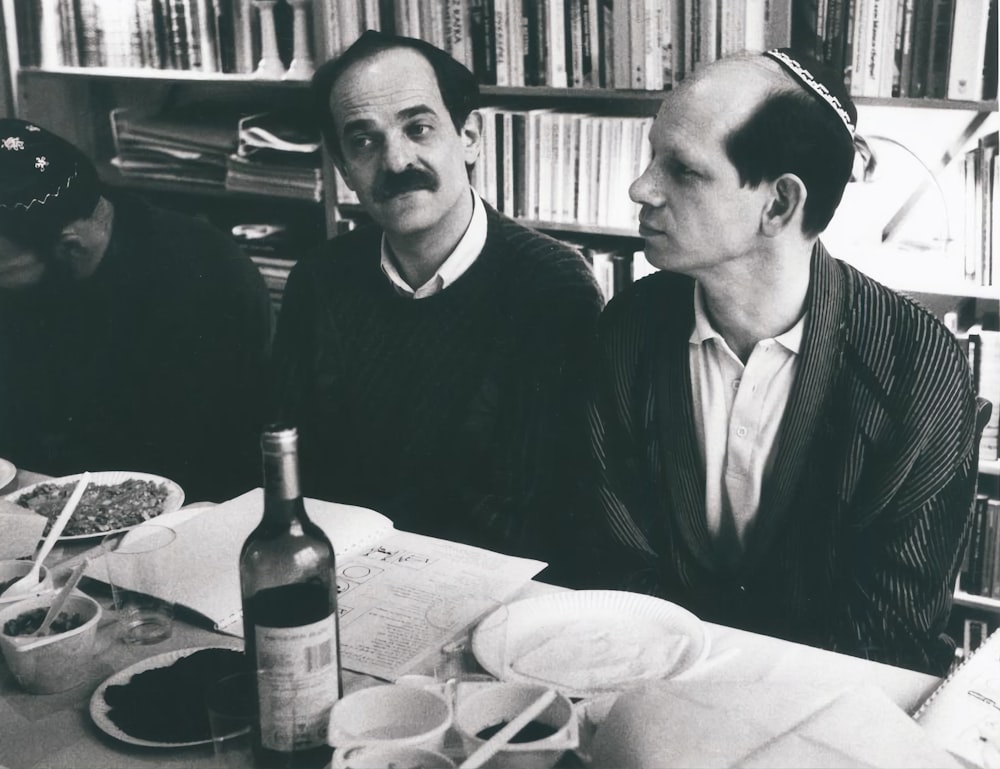 a couple of men sitting at a table with food and drinks