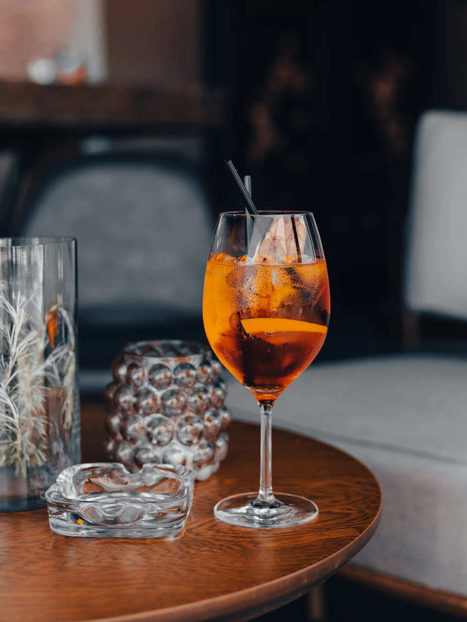 Wooden table with orange liquid-filled glass, white flowers, and cigarette ashtray nearby
