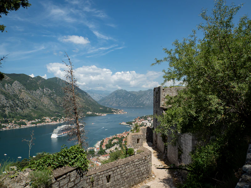 A stone path along Kotor's old fortification walls high above the bay, with mountains beyond