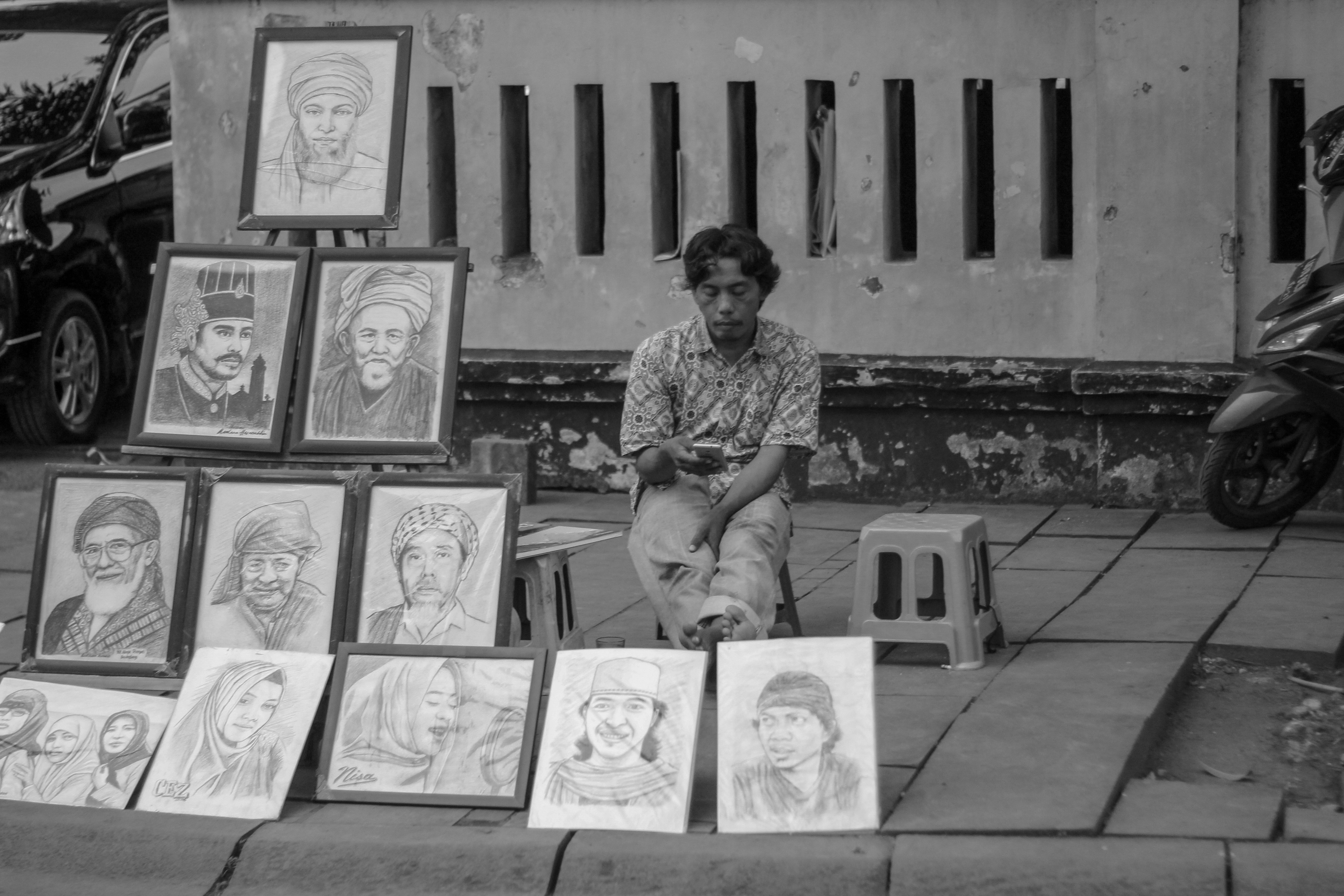 a person sitting on a sidewalk with a bunch of photos on the wall